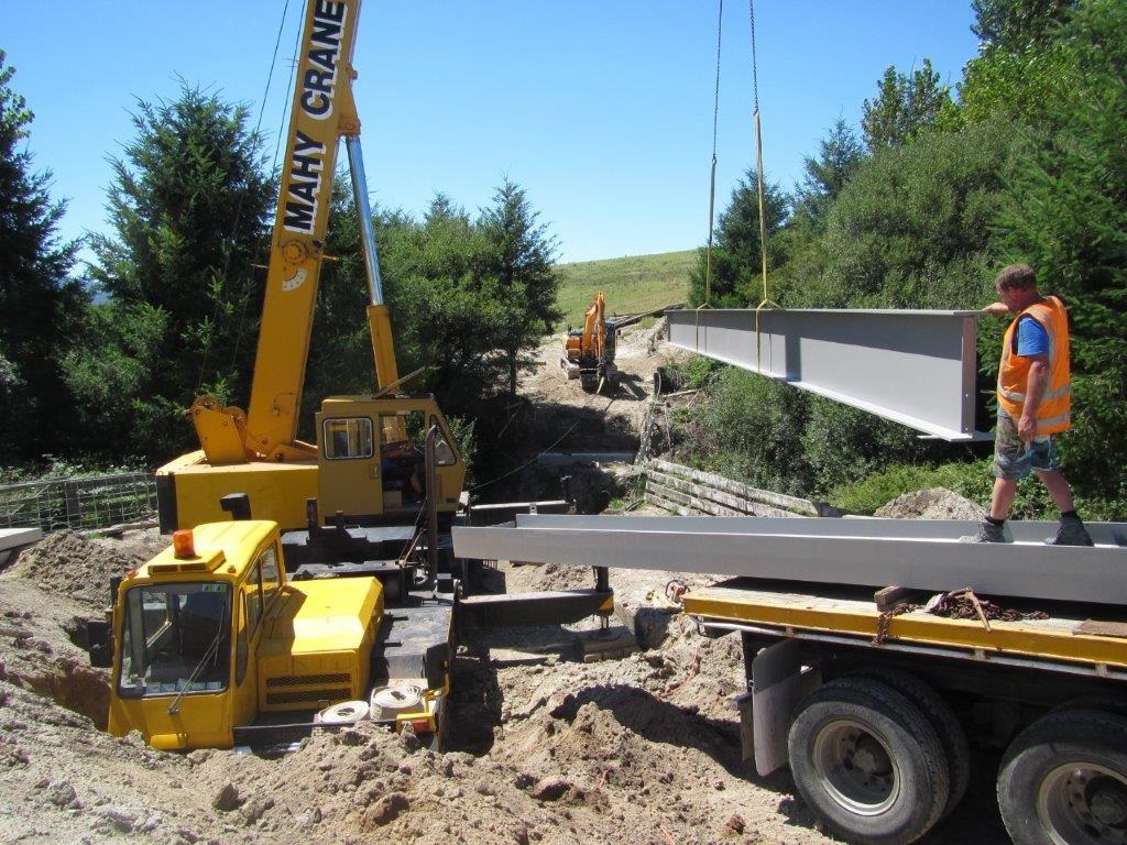 Mahy Crane Hire mobile crane lifting a large steel beam on a rural bridge construction site