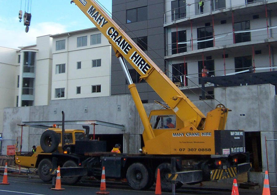 Mahy Crane Hire yellow mobile crane working on a construction site beside a building under construction