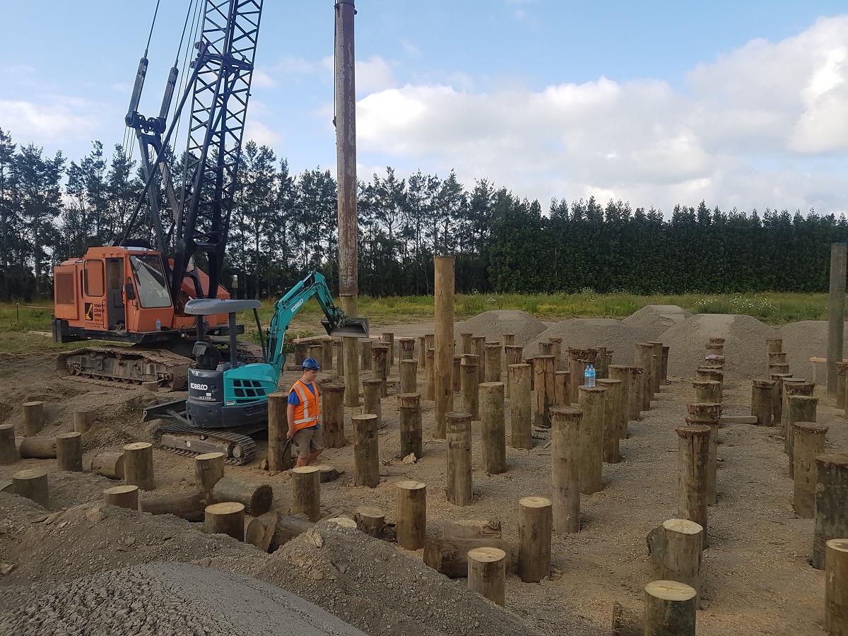 Pile driving site work with timber foundation piles, crawler crane and excavator